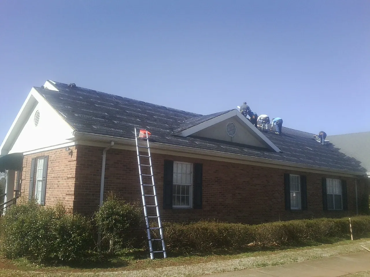 Crew tearing shingles off a brick ranch roof with a ladder set — Metal Roof Repair work by our crew in Pennville