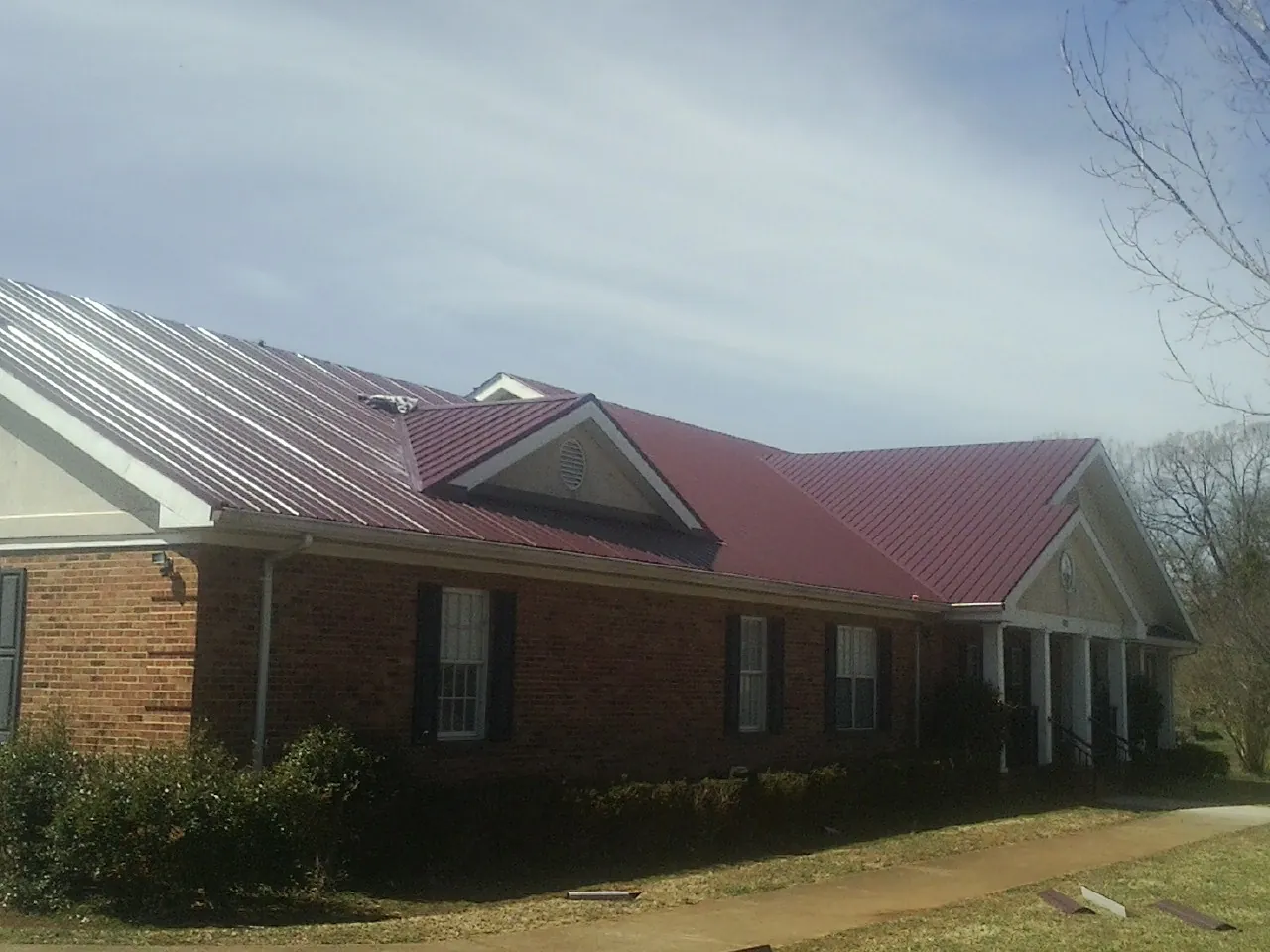 Red metal roof with gabled entries on a long brick building, from a Hail Damage Roof Repair job in Pennville
