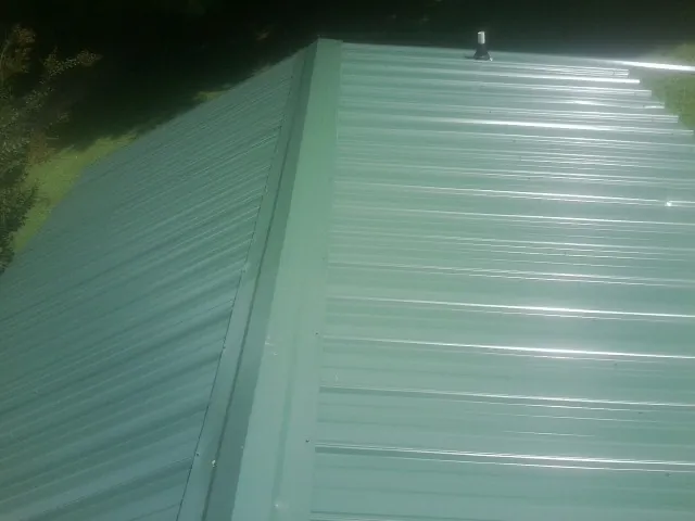 New green metal panels meeting at the ridge of a roof — Flat Roof Repair work by our crew in Pennville