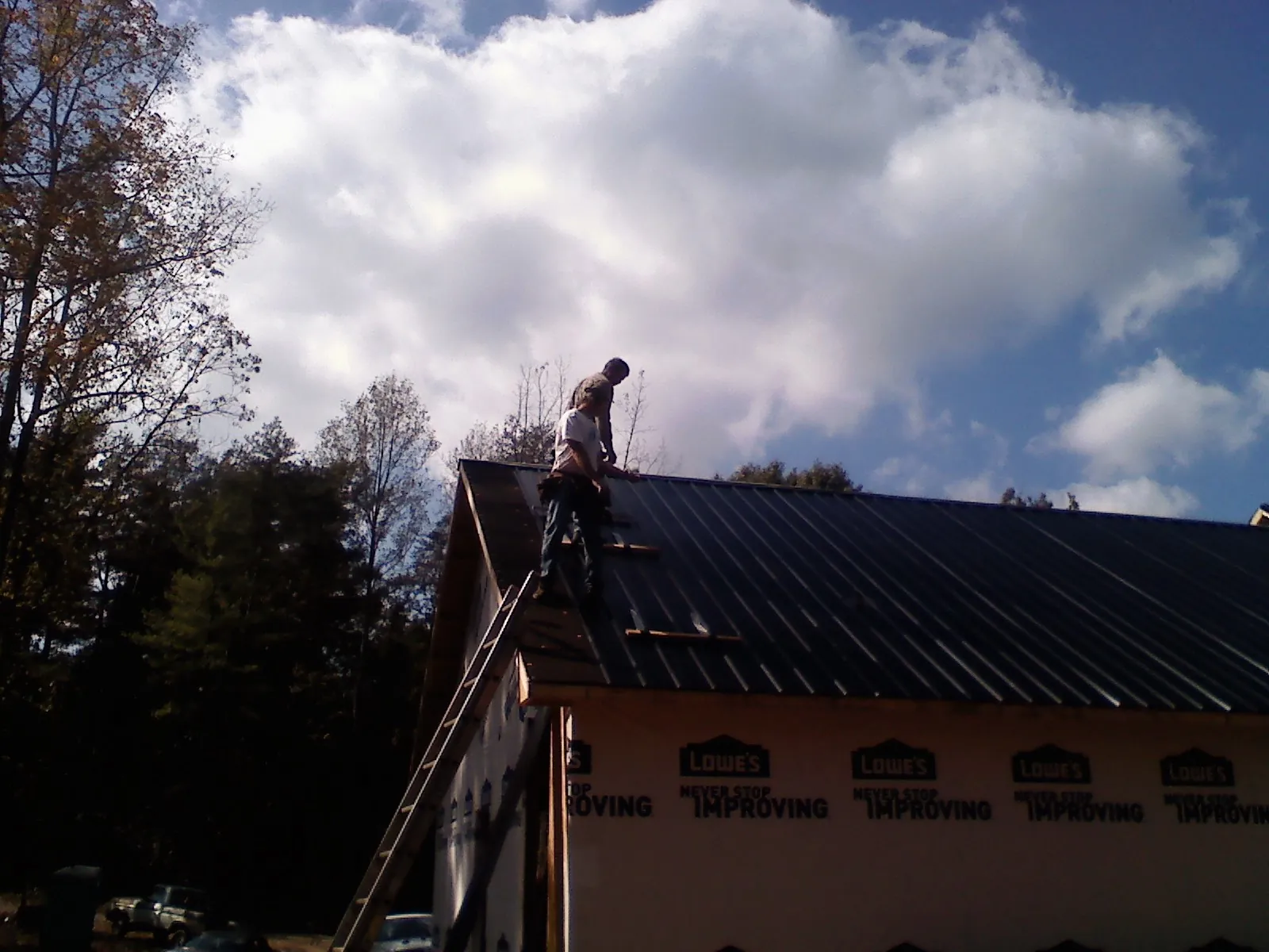 Roofer fastening dark metal panels high against a cloudy sky, from a Roof Inspection job in Pennville
