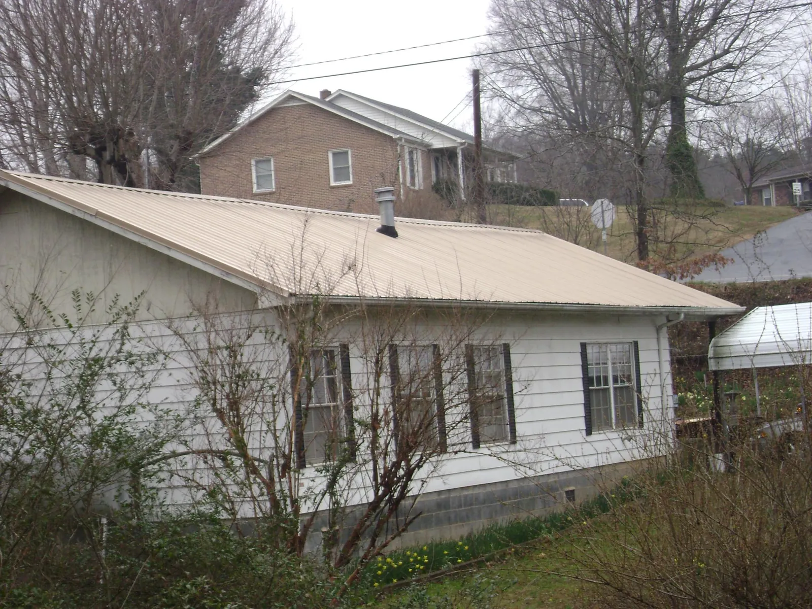 Tan metal roof on a white sided house set into a hillside — Commercial Roofing by Roofing Brothers in Pennville
